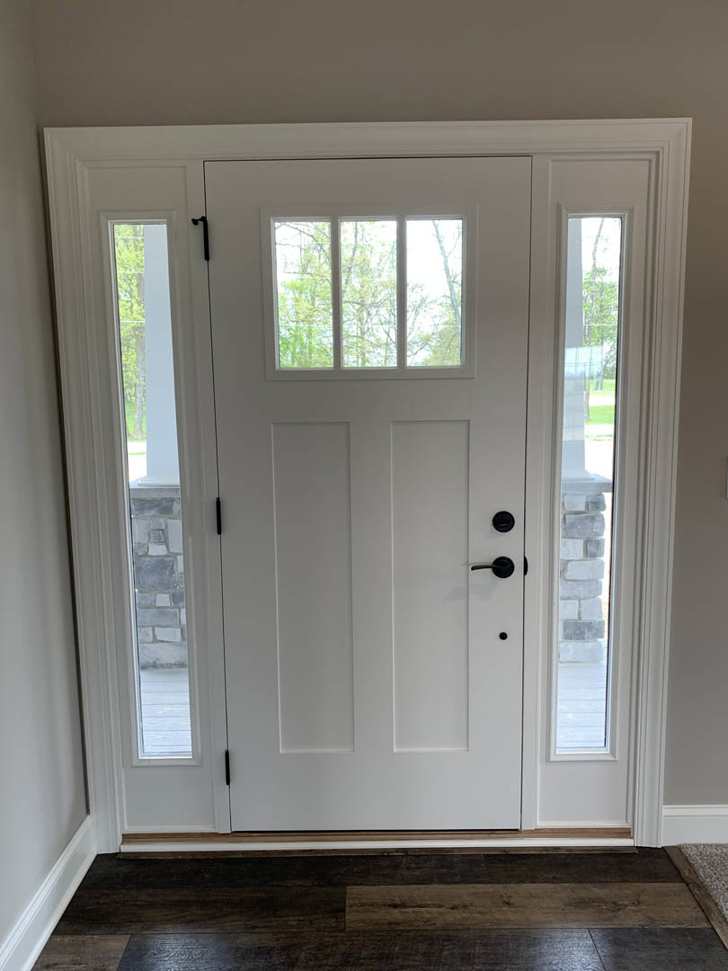 White door with glass panes and black handle, stone wall detail, wooden floor, trees visible through window