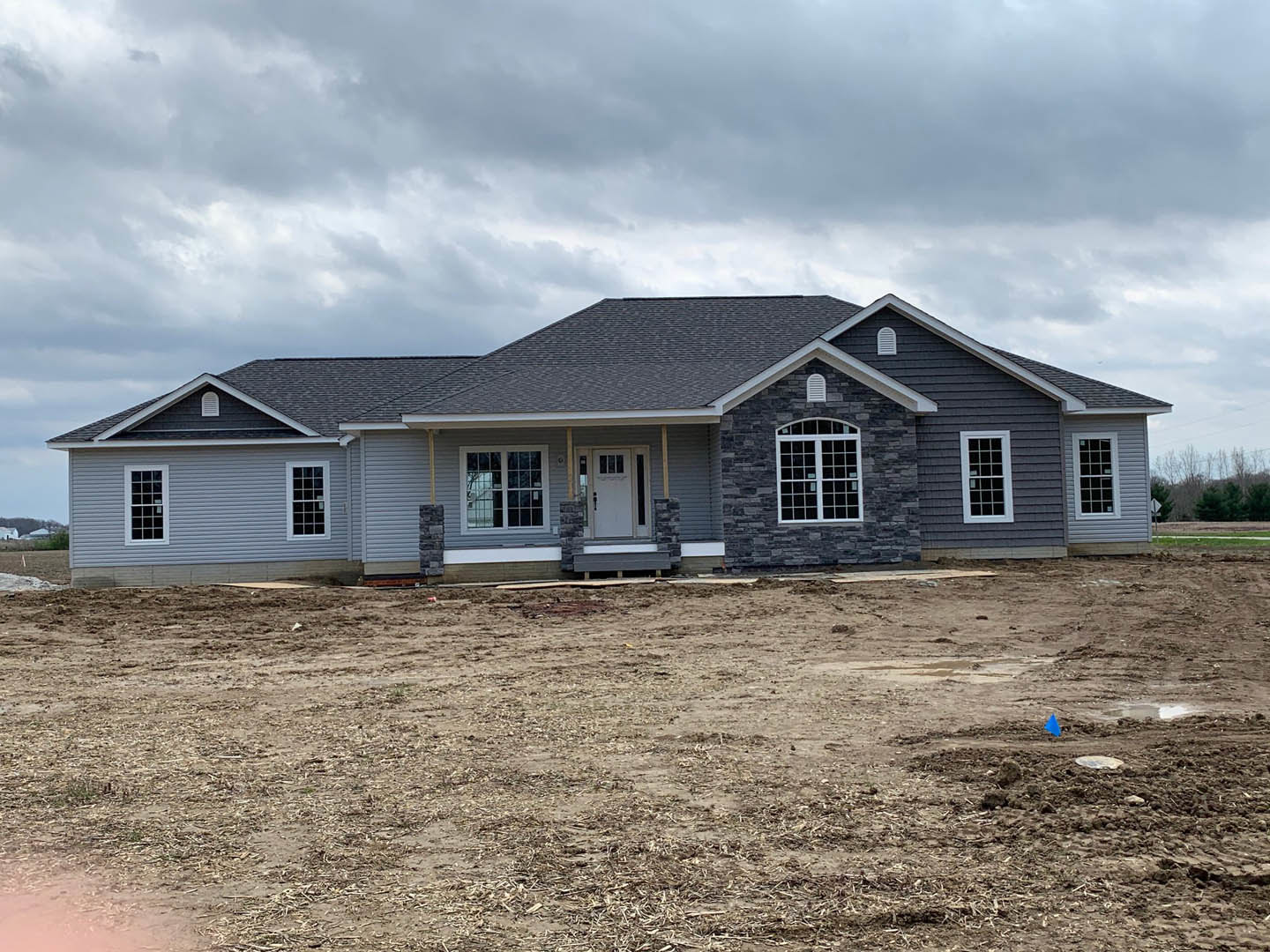 Two-story house with white door and multi-pane windows, surrounded by a dirt field under a cloudy sky