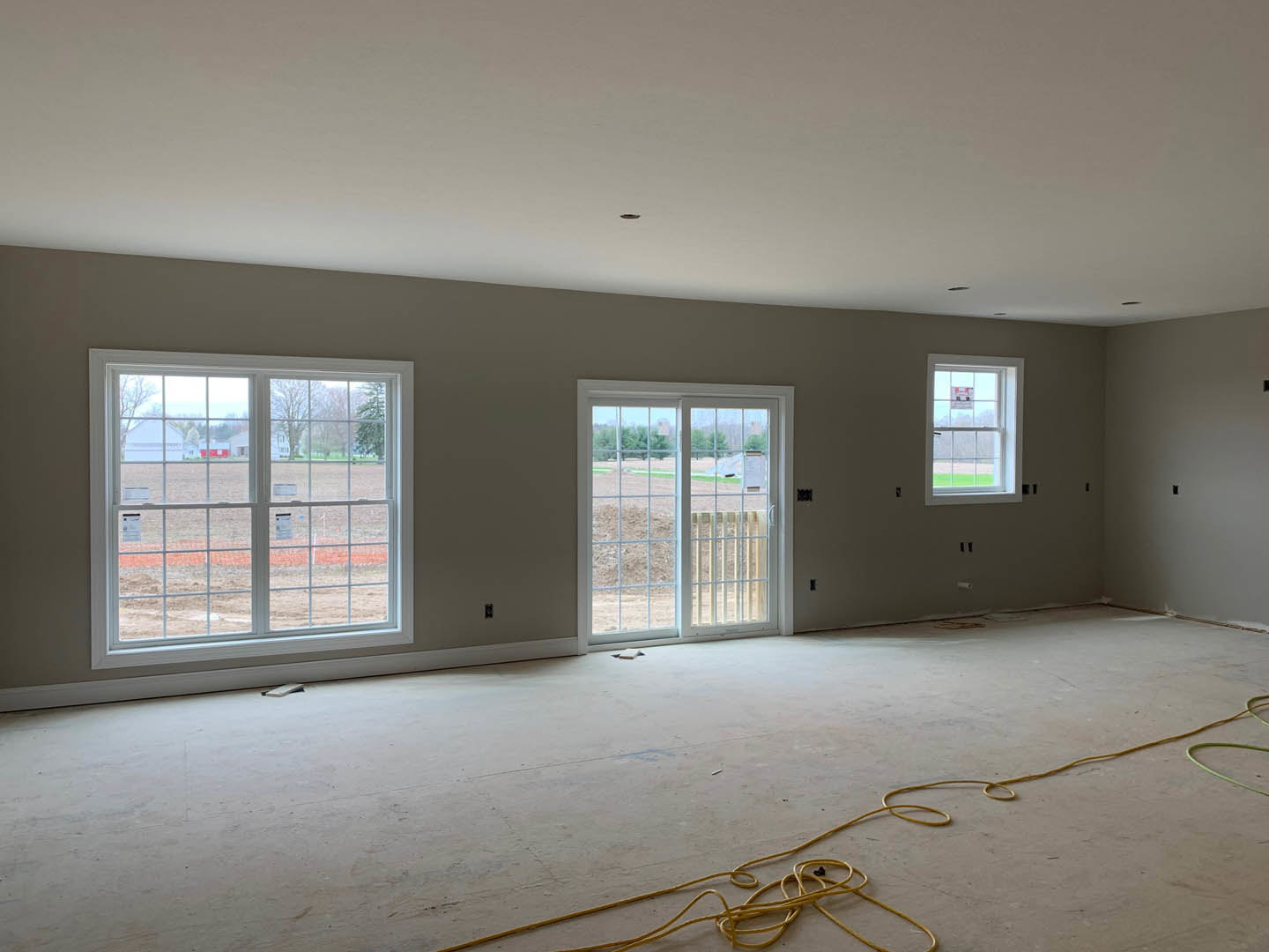 Bright room with white plaster walls, multiple windows overlooking a grassy field, sliding glass door, yellow rope lying on the floor, white ceiling with a visible spot, and a