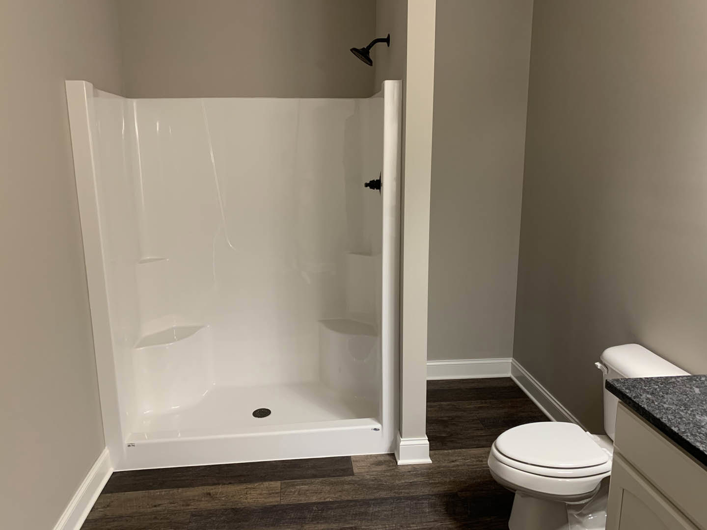 Modern bathroom featuring a white tiled shower with chrome showerhead, adjacent white toilet, light-colored countertop, and neutral wall finishes