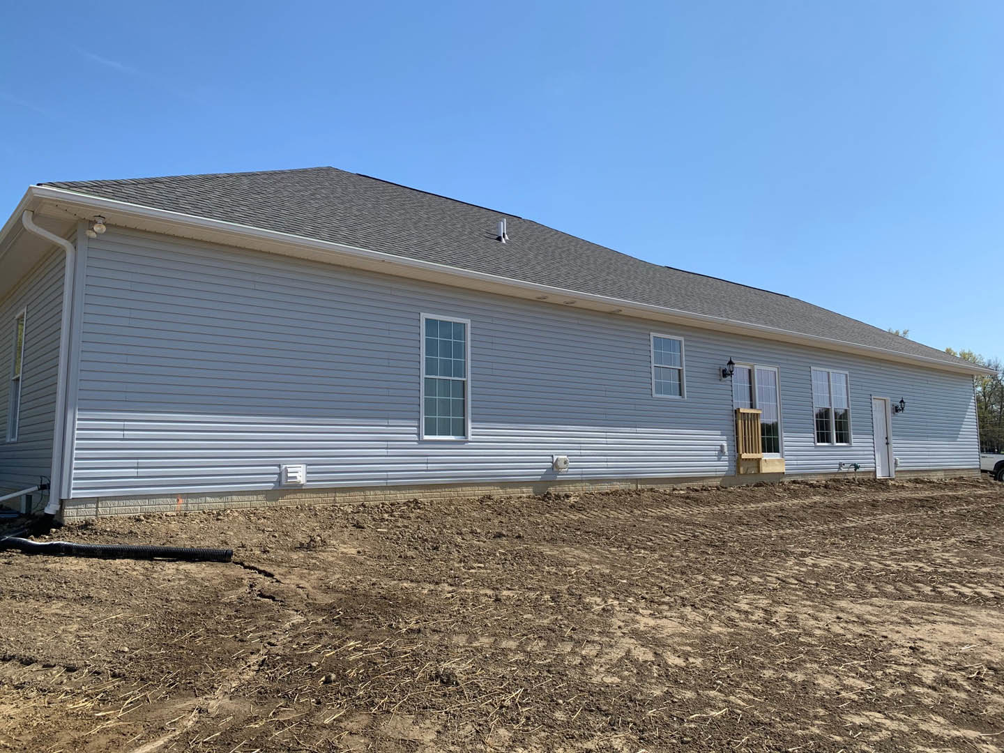 Modern house with metal siding, multiple square-paned windows, and a dirt yard under a clear blue sky