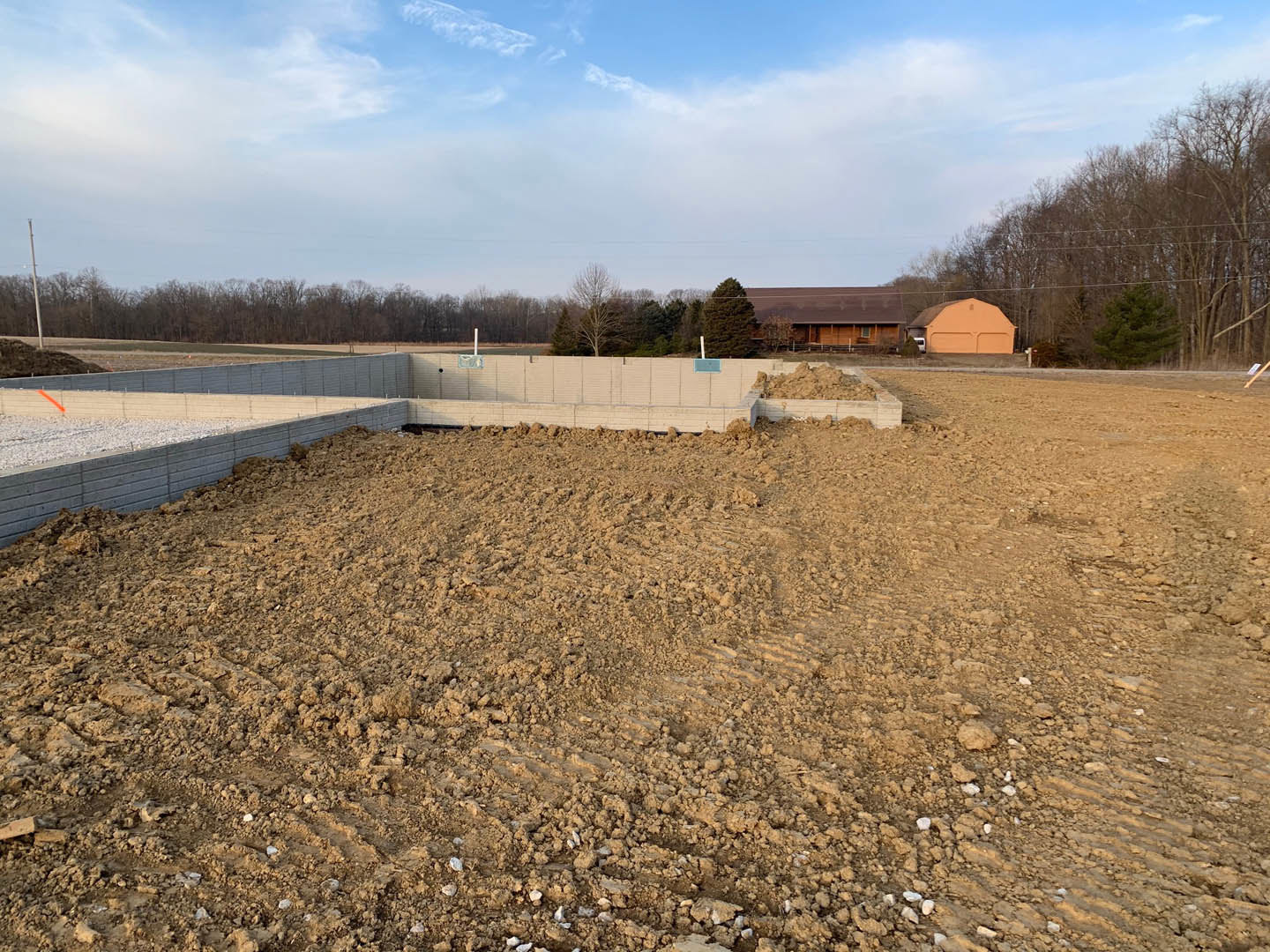 Dirt field with a basketball hoop, low building in the background, metal fence, blue sky with scattered clouds