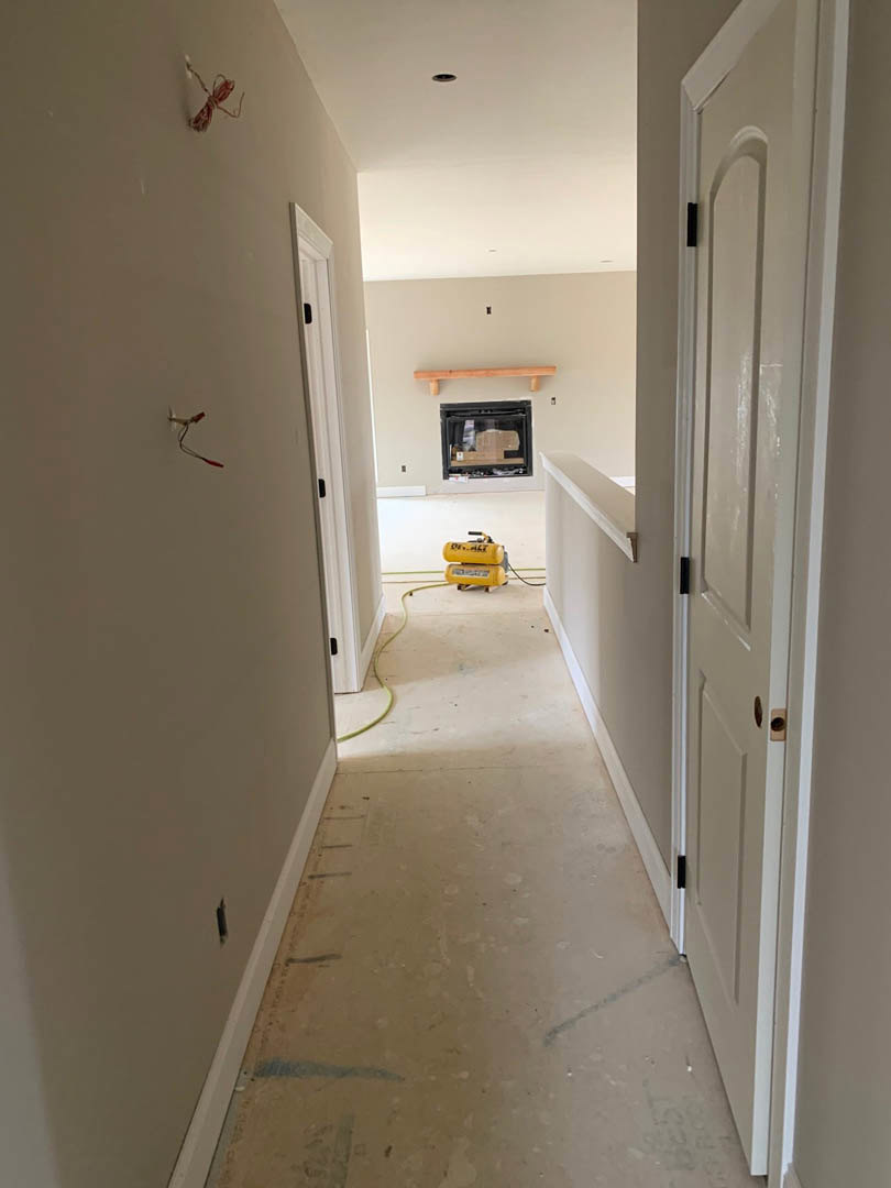 Hallway with plaster walls and light flooring, yellow gas cylinder near a glass window with wood trim, white door with black handle, electrical plug, string tied to wall