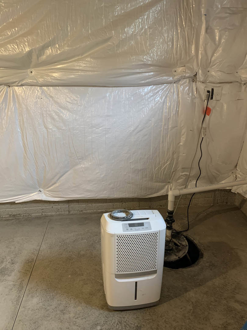 White rectangular appliance with buttons and screen, partially covered in clear plastic, positioned against a white wall on a light-colored floor.