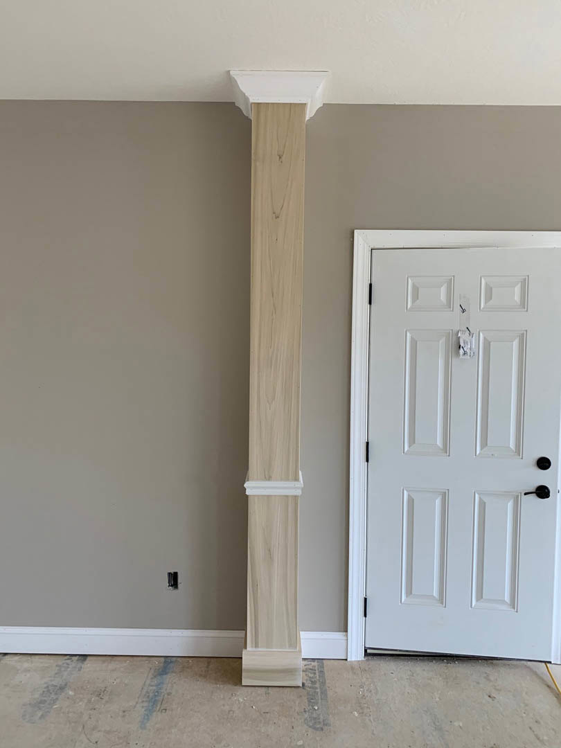 White door with black handles beside a white pillar, wood panel flooring, white paneled walls with black trim, and white ceiling.