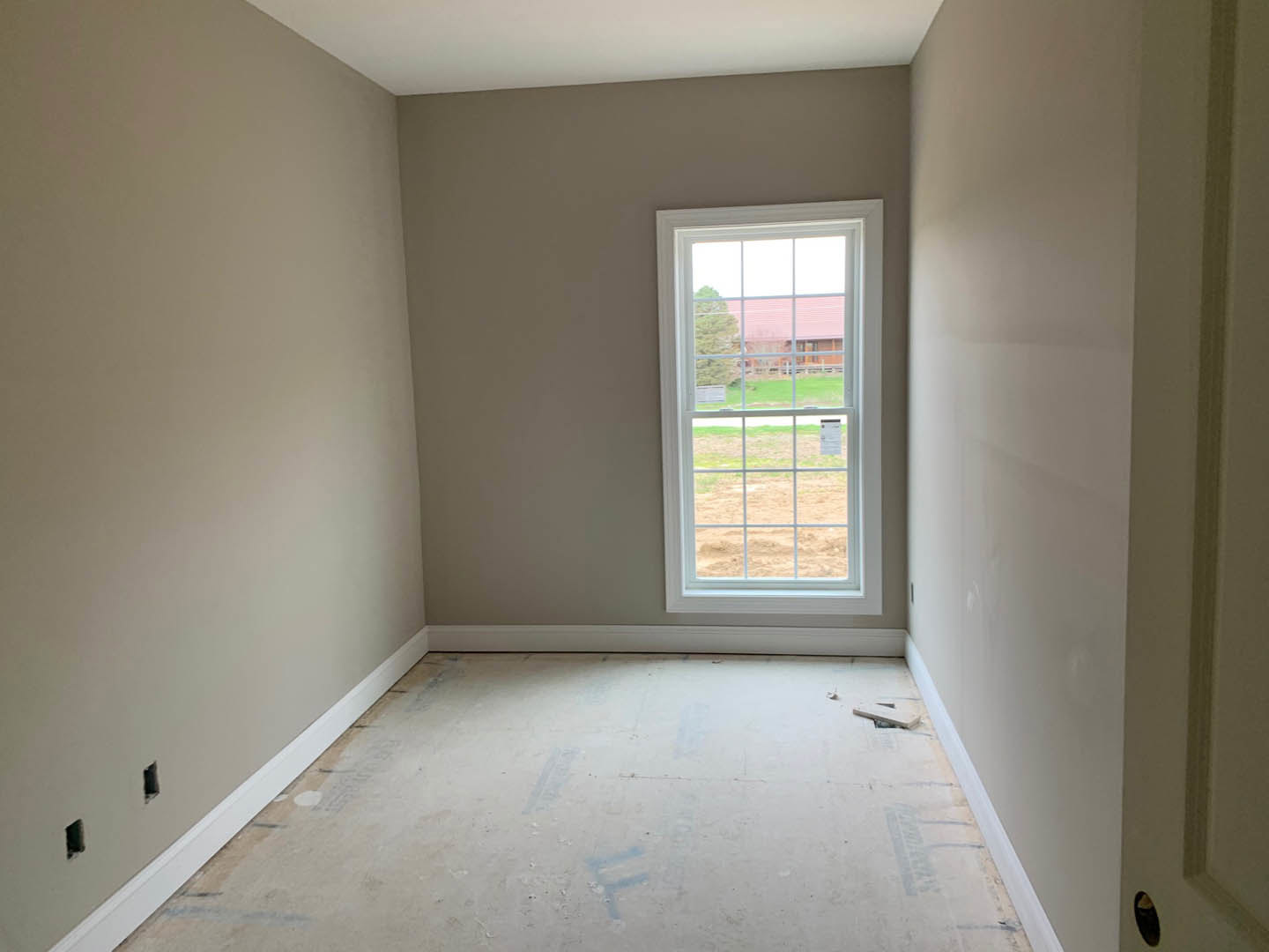 Concrete floor with blue paint, white walls, window with white frame overlooking farmland, ceiling light fixture
