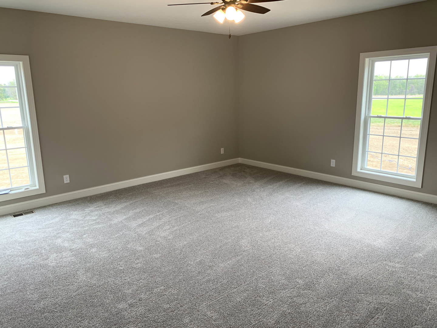 Neutral-toned room with grey carpet, white walls, ceiling fan with light fixture, and large window overlooking grassy field