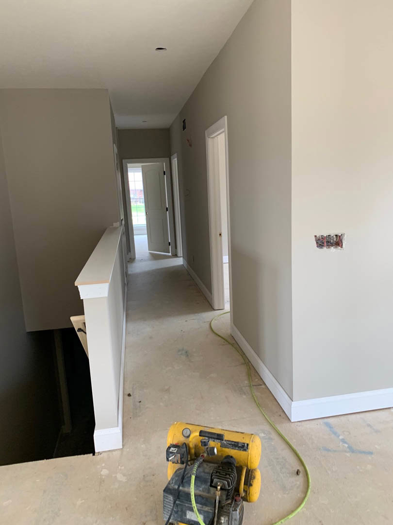 Hallway with white walls and flooring, yellow air compressor on the floor, glass door with black handle, white door frame, residential interior under construction