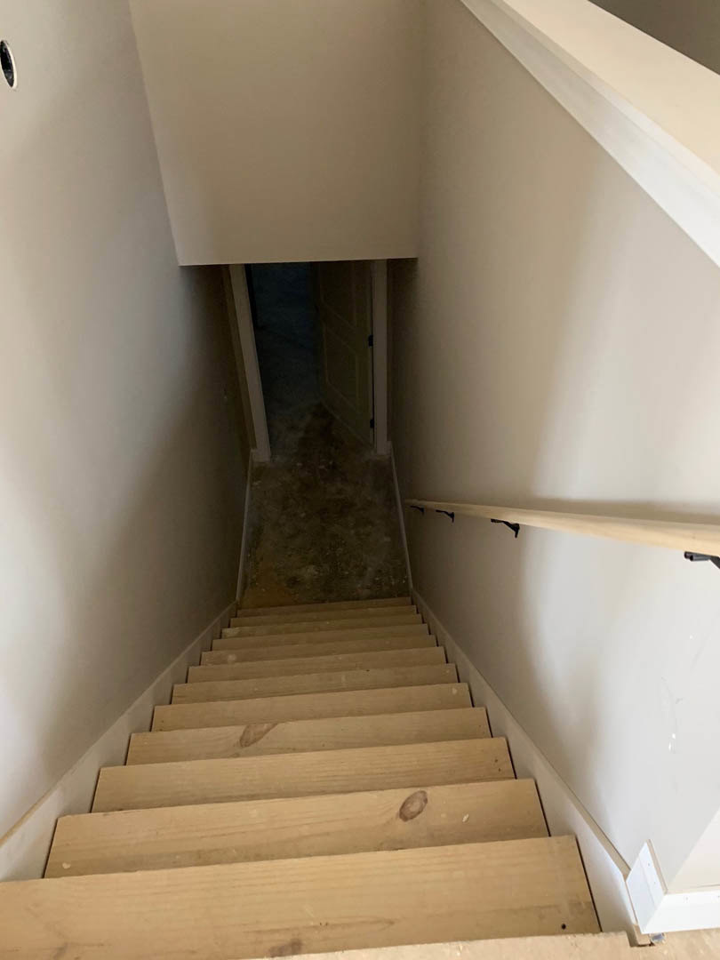 Wood staircase with metal handrail ascending toward a narrow hallway with plaster walls and a closed door, illuminated by soft indoor lighting