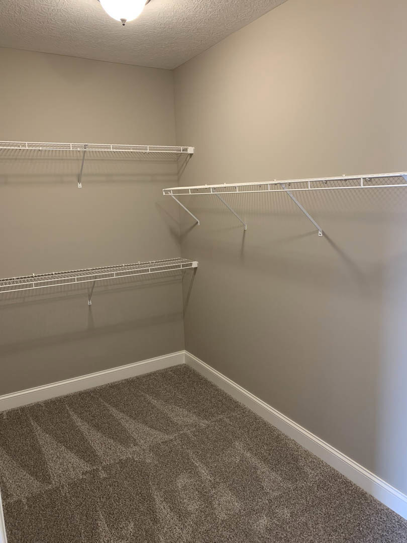 Carpeted room featuring white metal shelving, round ceiling light fixture, and white metal railing mounted on the wall.
