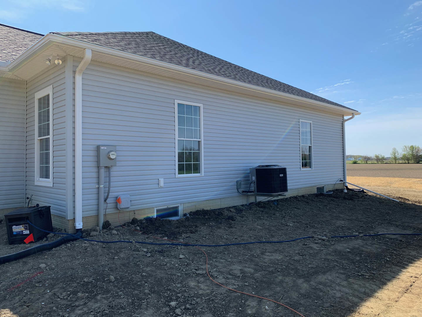 White siding home with large grassy yard, rectangular window, black outdoor heater box with hose attached, cloudy sky overhead