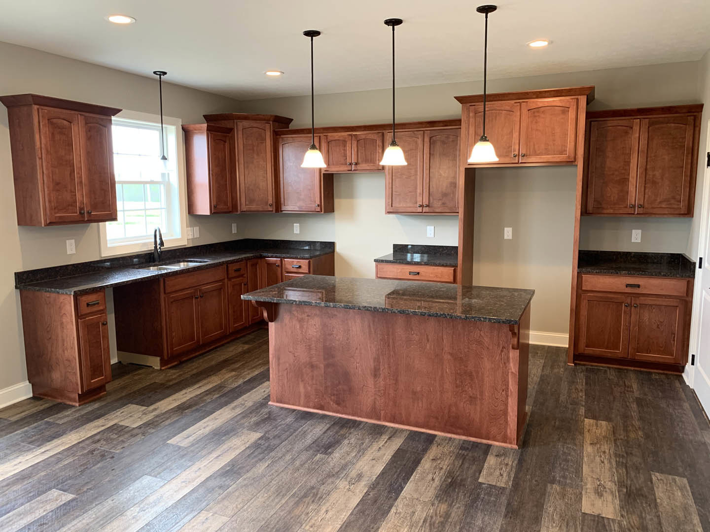 Kitchen with natural wood cabinets, matching wood plank flooring, marble countertop island, black metal faucet, and sunlight streaming through a window.