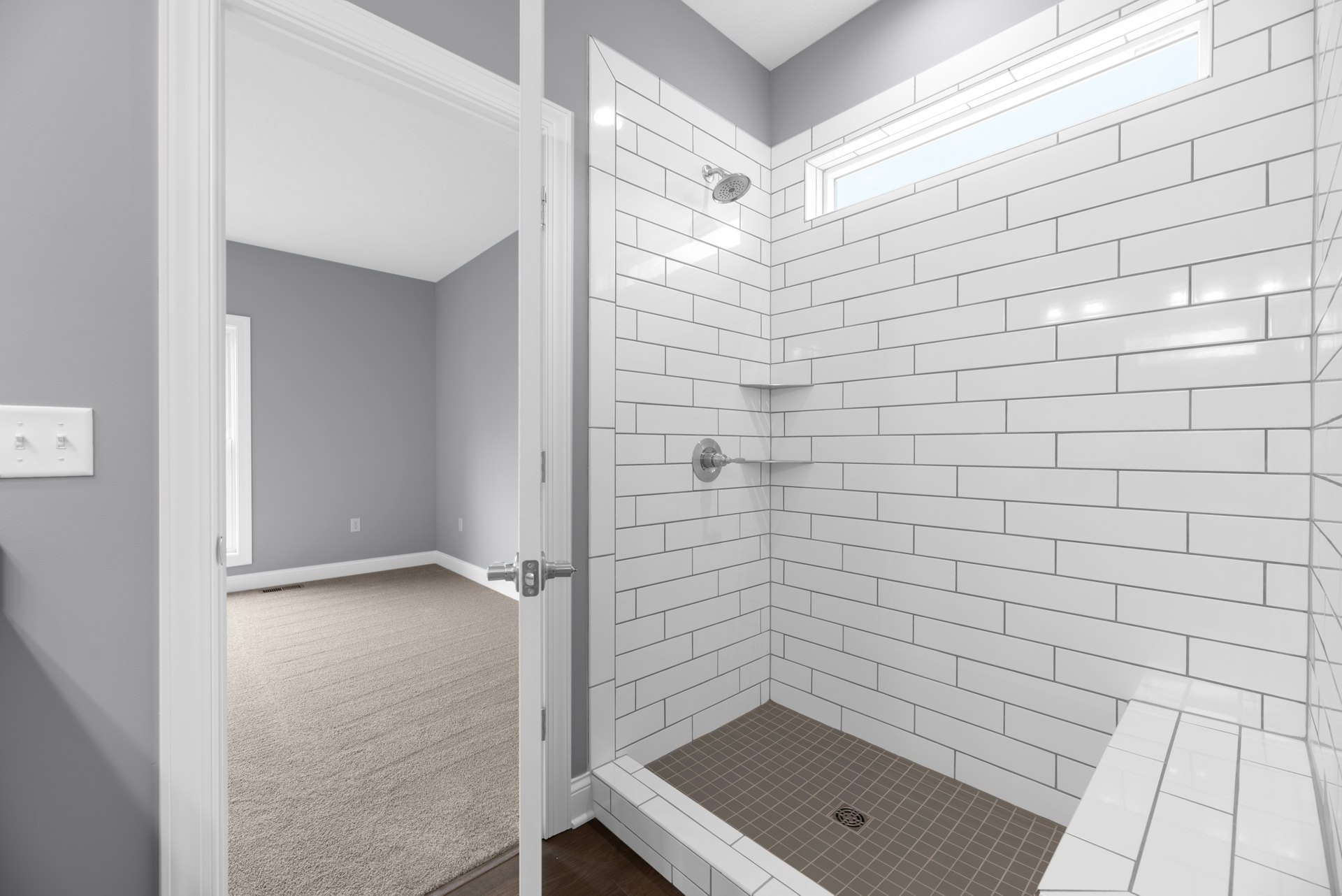 Bathroom with tiled shower floor, visible shower drain, white plaster walls, two-switch light plate, carpeted adjacent room, and close-up of door knob