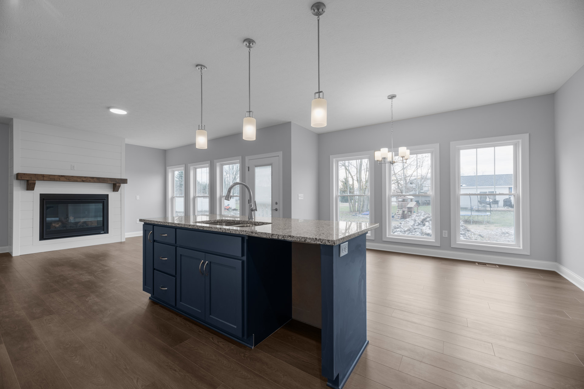 Spacious kitchen featuring a large granite island with wood flooring, white cabinetry, and a window overlooking the backyard; modern pendant lighting above the island and a