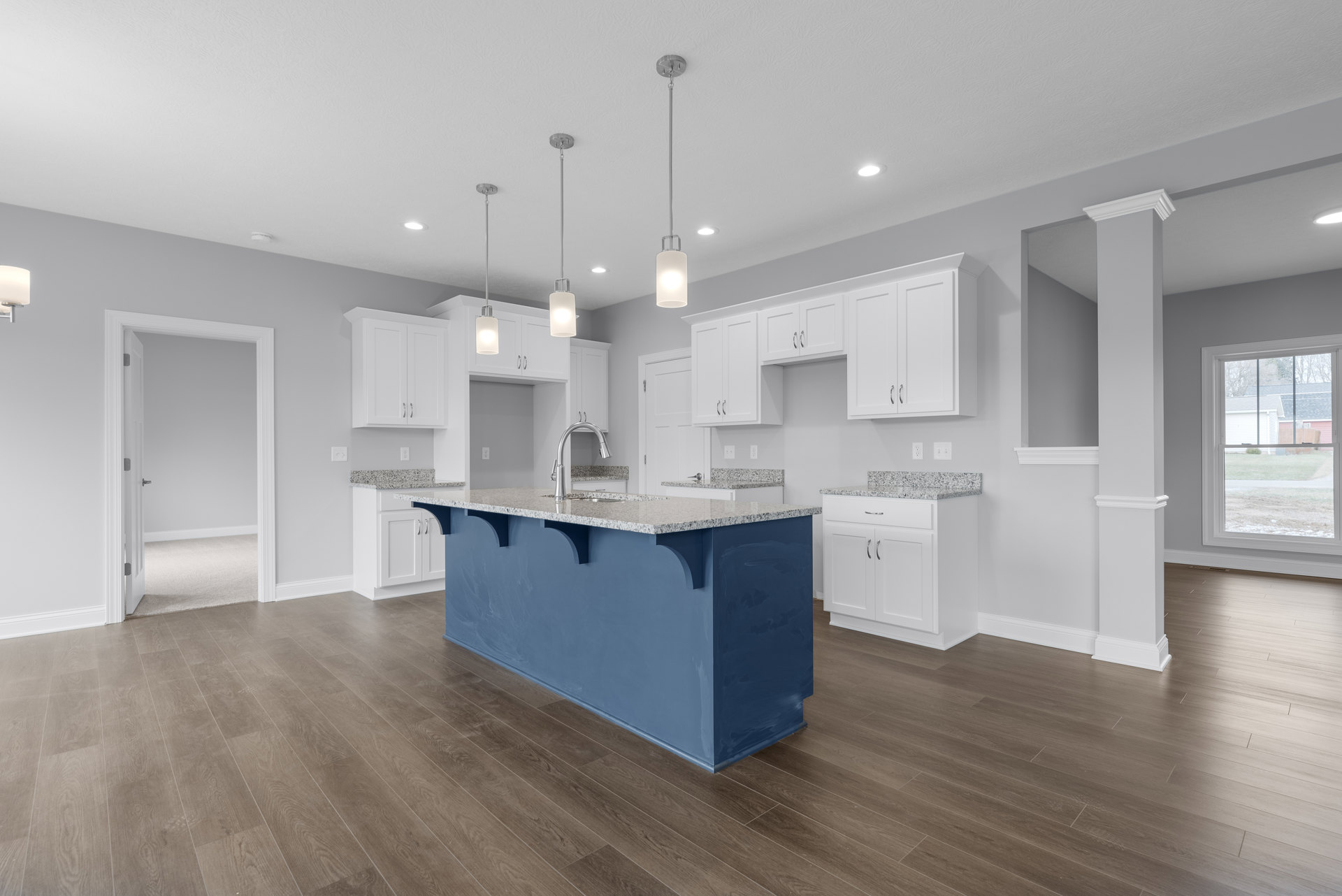Blue kitchen island with granite countertop, surrounded by white cabinets, stainless steel sink, and silver hardware; window overlooks neighboring house and lawn; white door with