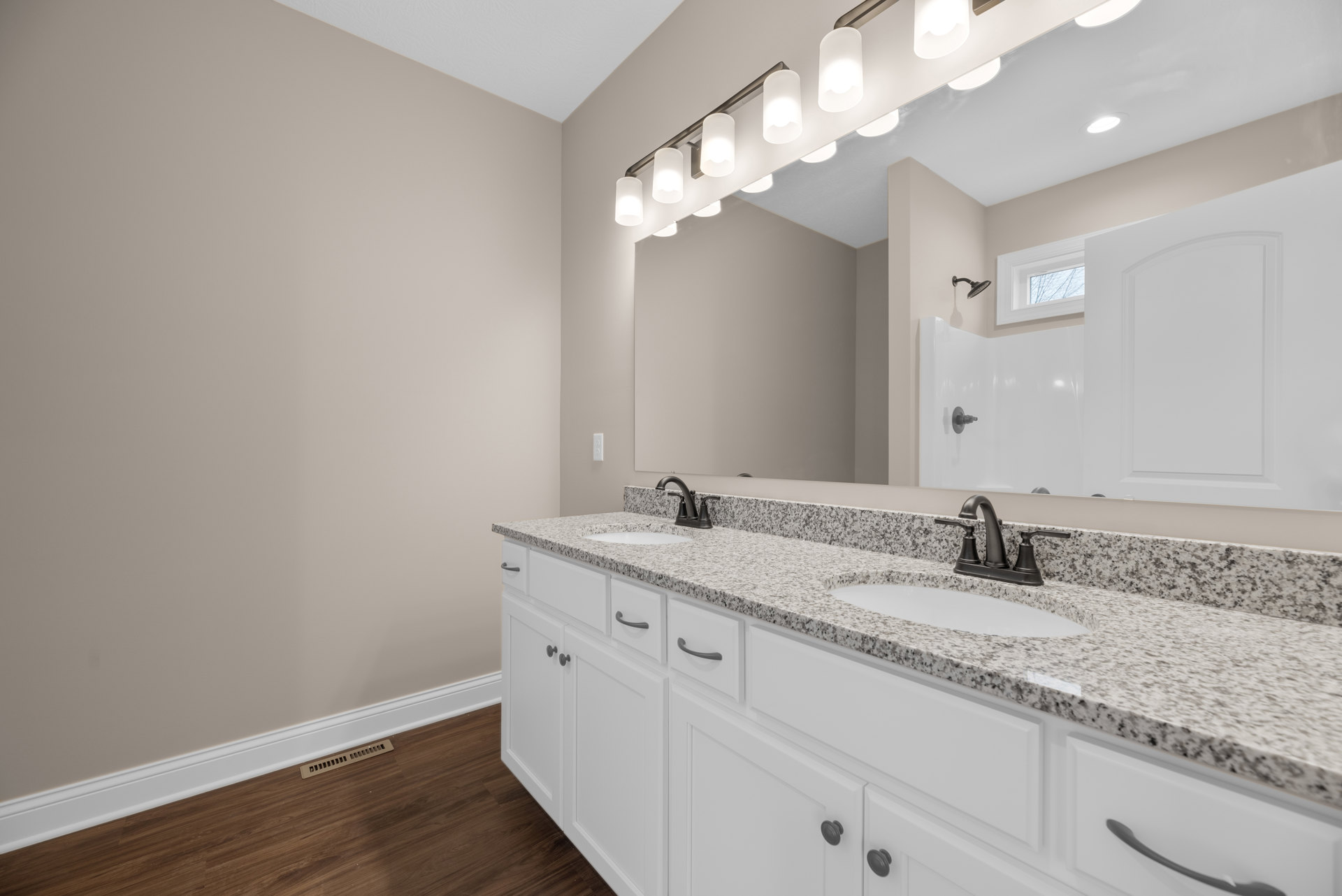 Double vanity bathroom with white sinks, chrome faucets, large framed mirror, row of wall-mounted lights above, light tile backsplash, and white cabinetry below.