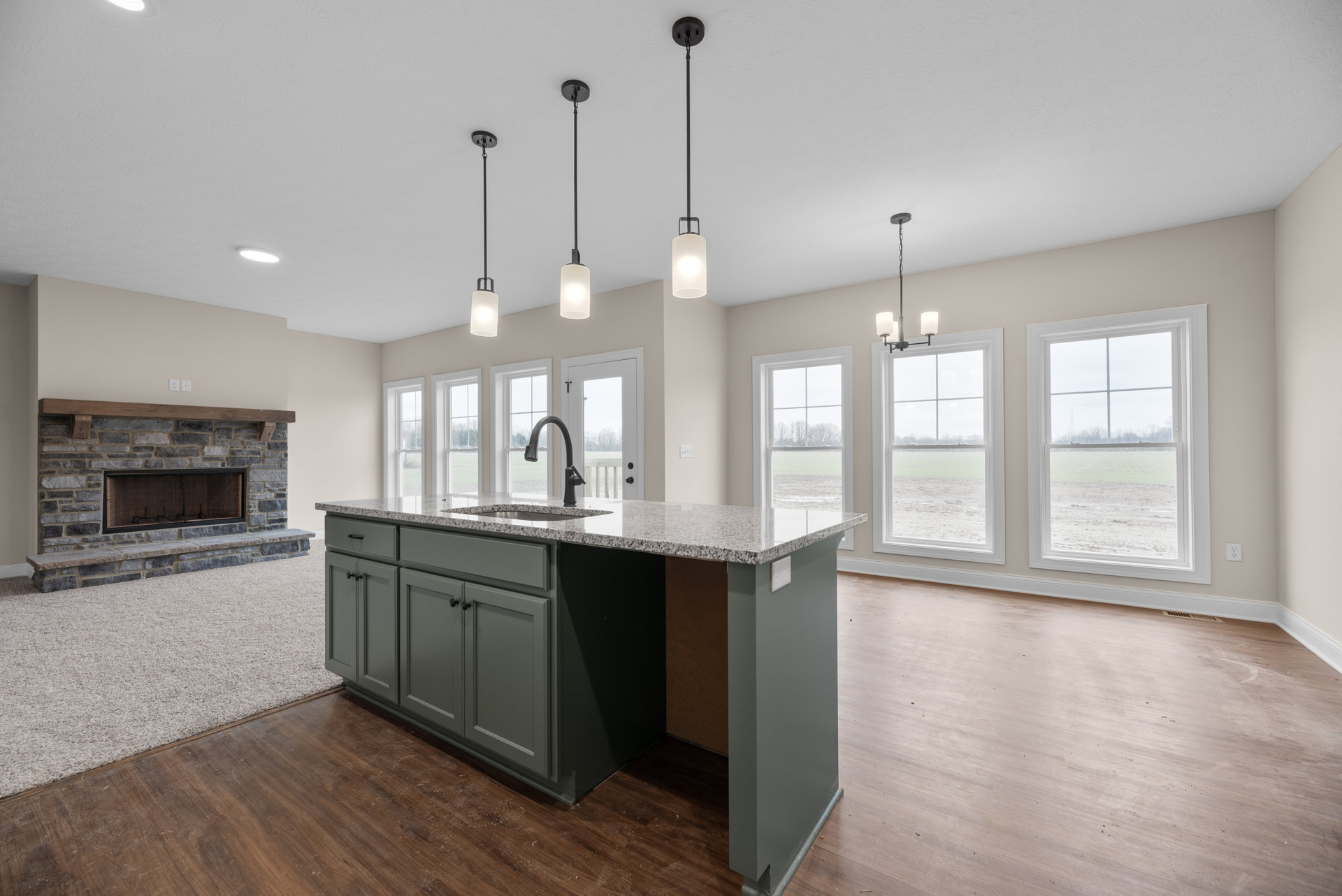 Kitchen with stone fireplace featuring wood beam mantel and glass window, farmhouse sink set in light countertop, cabinetry along walls, window overlooking field, black pole light