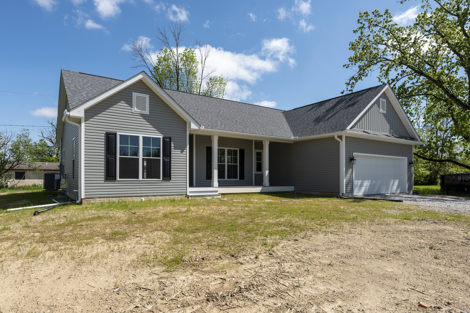 Two-story home with gray siding, white-framed windows, covered front porch, paved driveway, and mature tree in landscaped yard