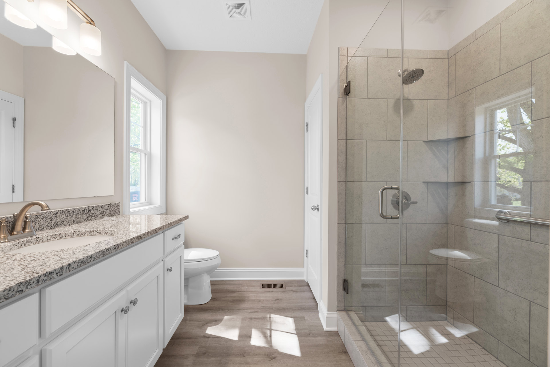 Modern bathroom featuring a glass-enclosed shower, white porcelain sink with chrome faucet, closed toilet, tiled walls, and a window overlooking greenery.
