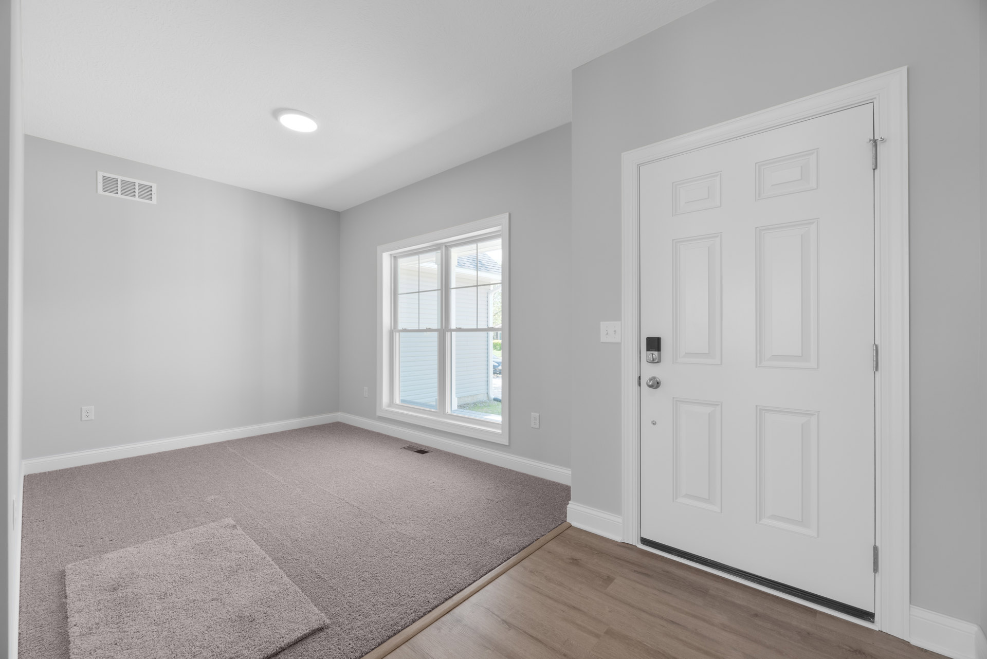 White carpeted room with white paneled door, white ceiling light fixture, and window with white trim