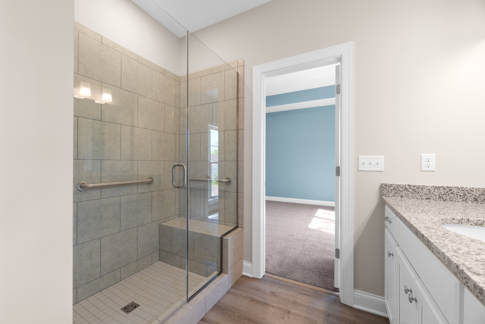 Bathroom featuring a glass shower enclosure with built-in bench, white countertop with undermount sink, tile flooring, and visible light switches and outlet on the wall.