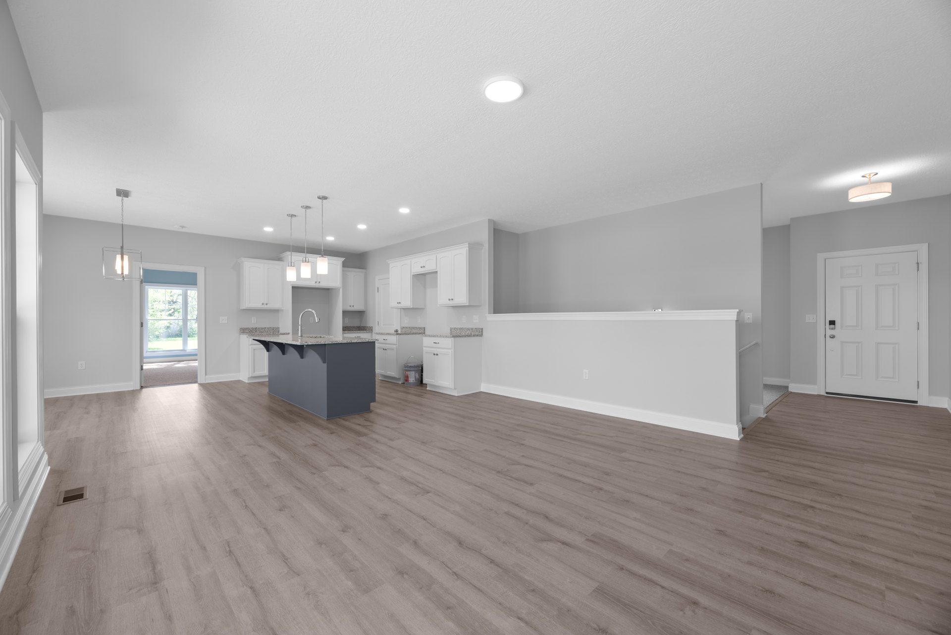 Spacious kitchen and living area with hardwood flooring, central kitchen island featuring granite countertops, white paneled door with lock, recessed ceiling light, smooth plaster
