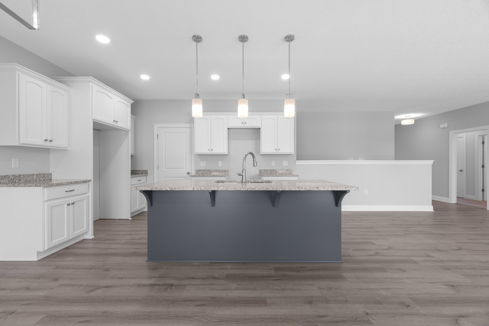 Spacious kitchen featuring a large granite island with built-in sink and silver faucet, wood flooring, white cabinetry, open shelving, and white doors with metal frames and