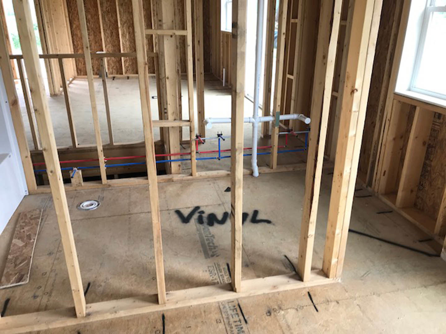 Unfinished room with exposed wood framing, visible plumbing pipes, window, and construction materials