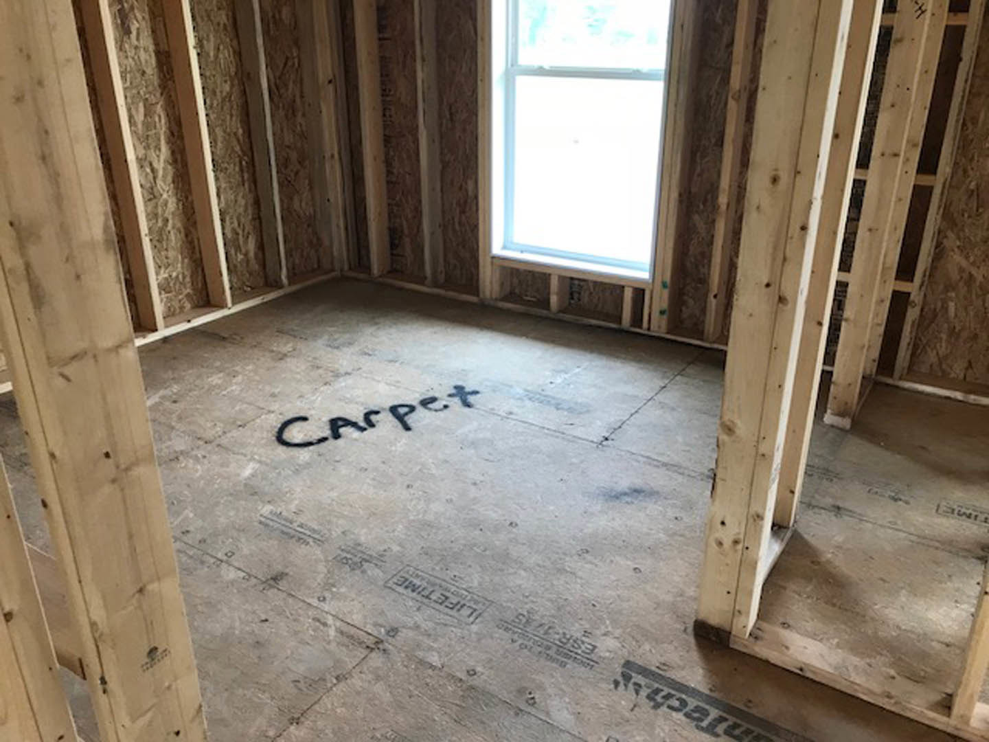Wood-framed room under construction with exposed beams, concrete floor, and window letting in natural light