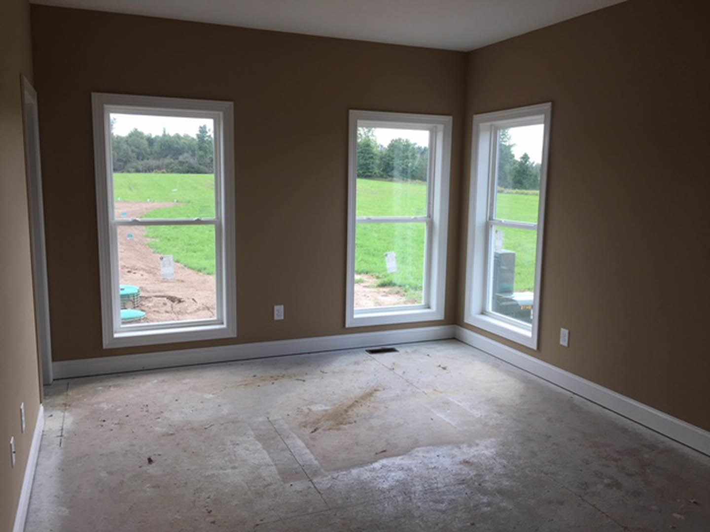 Spacious room with large windows, concrete flooring, plaster walls, and views of a green lawn and open field