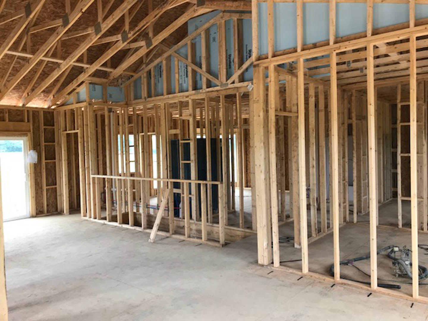 Wood framing and exposed beams inside a house under construction, unfinished ceiling and walls with visible lumber and building insulation.