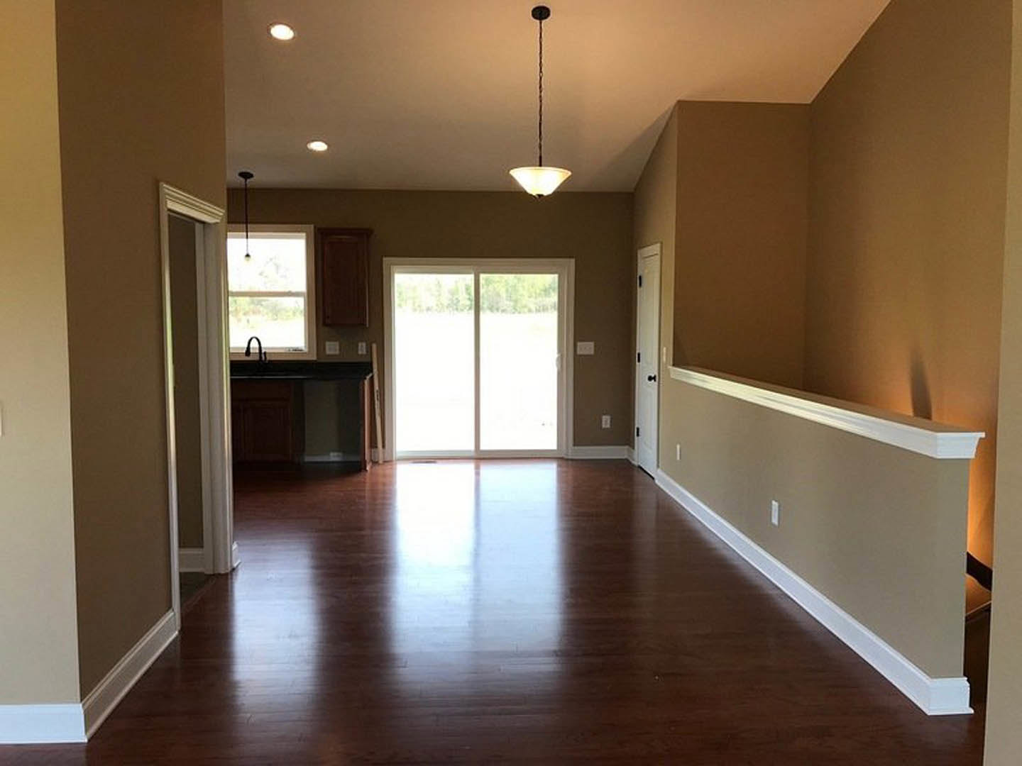 Hallway with white sliding glass door, hardwood flooring, white walls, recessed lighting, and large window at the end.