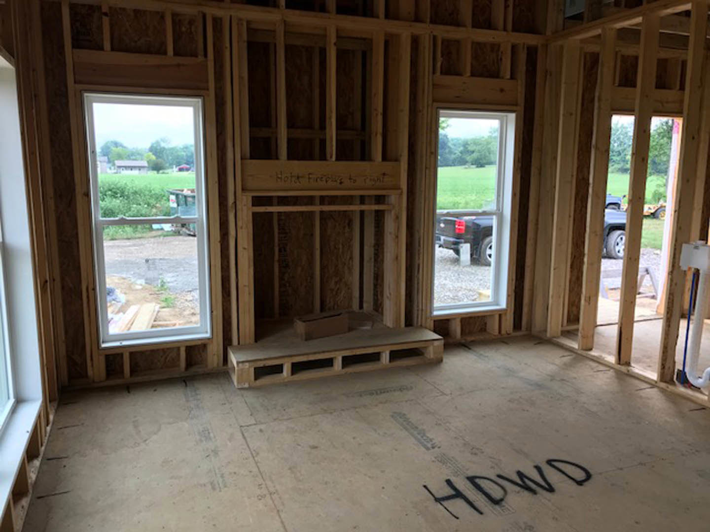 Living room featuring large windows, stone fireplace, hardwood floors, and exposed wood beams