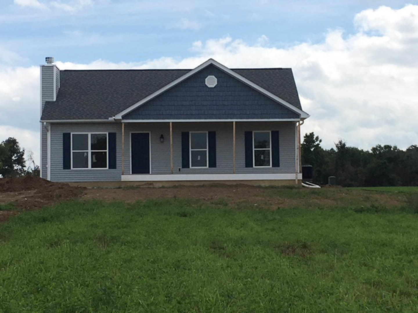 Two-story house with blue roof, white siding, large front windows, covered porch, and manicured green lawn under partly cloudy sky