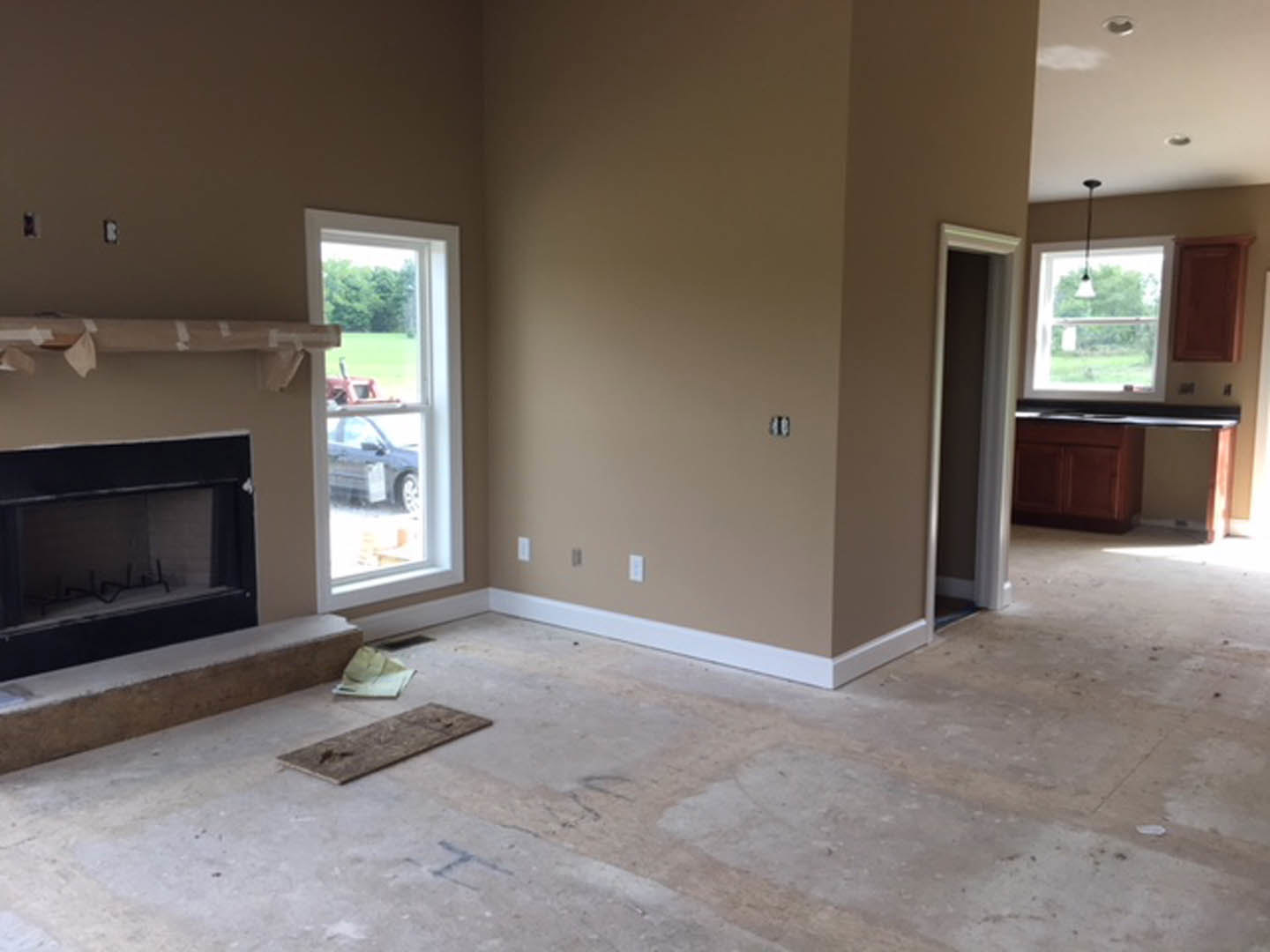 Living room featuring a black fireplace with glass window, polished concrete floor, large windows, and plaster walls; wood plank and computer mouse visible in foreground.