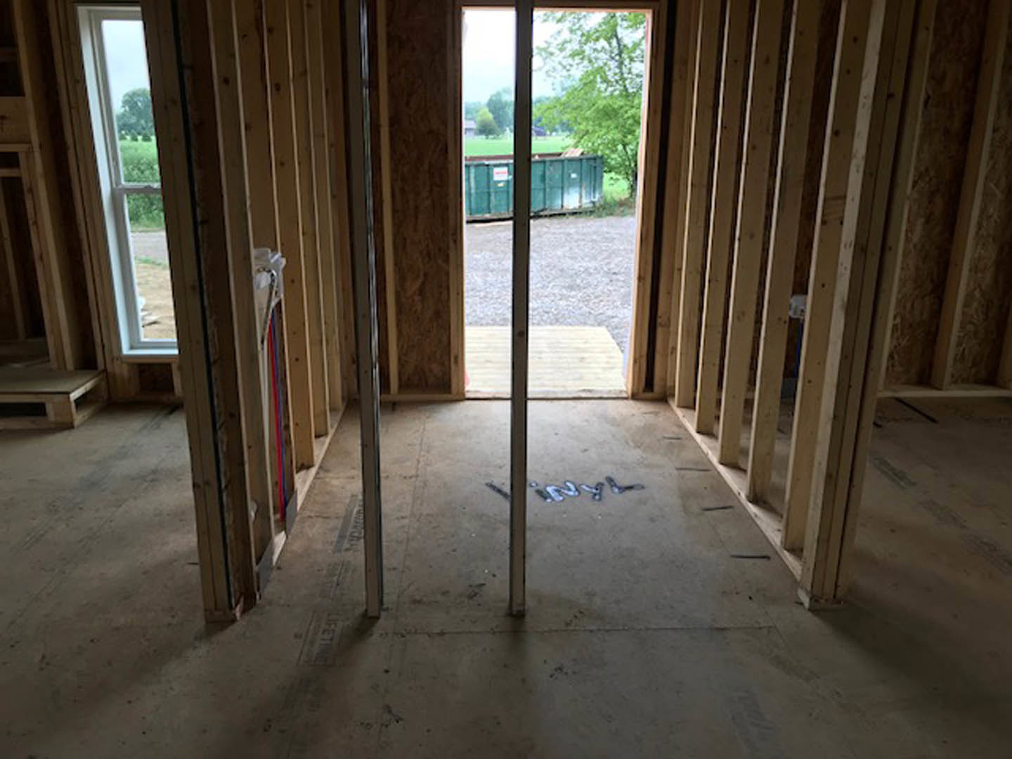 Concrete floor with metal support poles, wooden pallet, green container, door, and window in an unfinished room