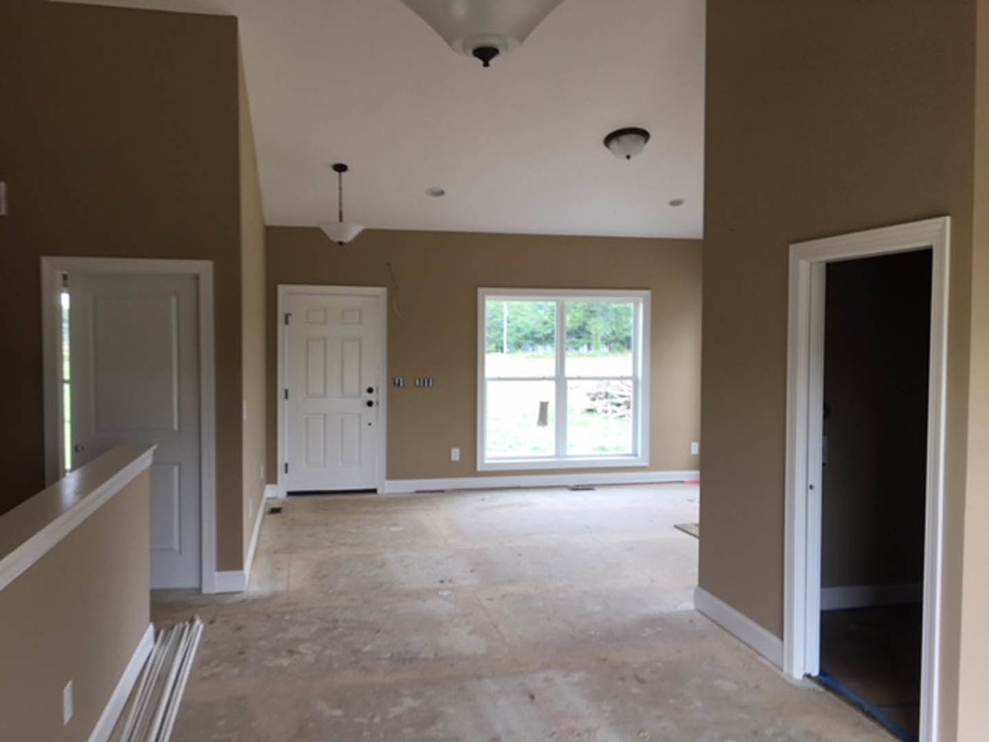 White paneled door with black hardware set in a white wall, large window with outdoor view, dark accent wall, light wood flooring, recessed ceiling light, simple crown molding