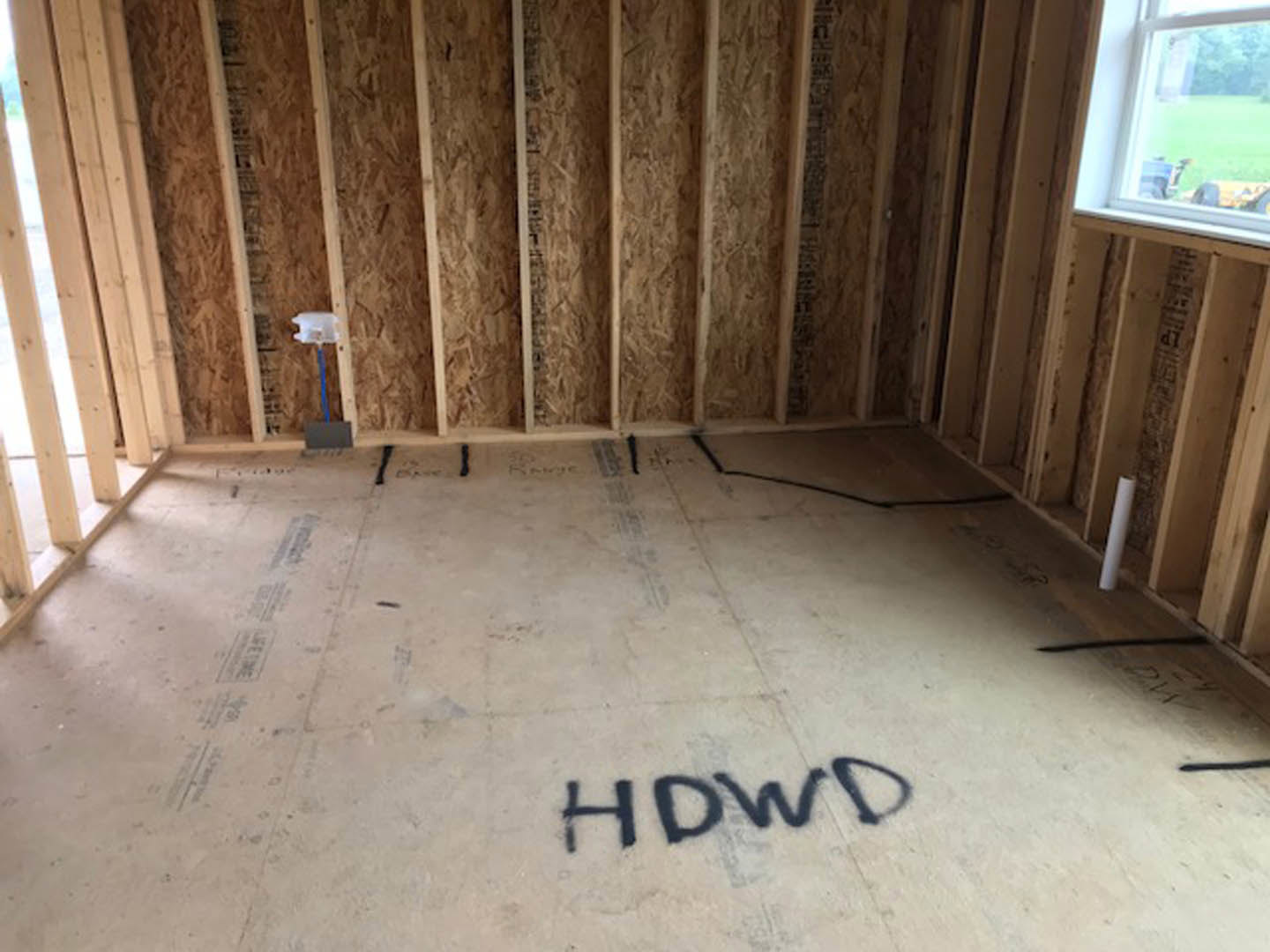 Room with vertical wood plank walls, concrete floor featuring black lettering, white support pole, window overlooking green lawn, blue handle attached to wooden pole