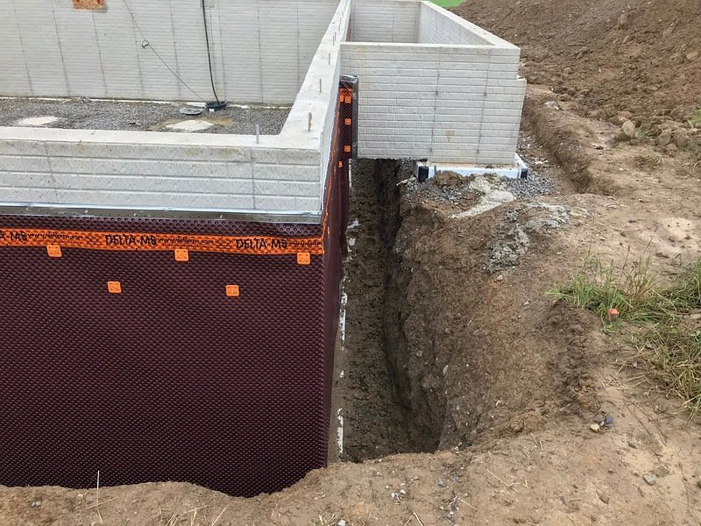 Excavated dirt field with partially built white brick foundation, orange safety tape, and exposed hole in ground