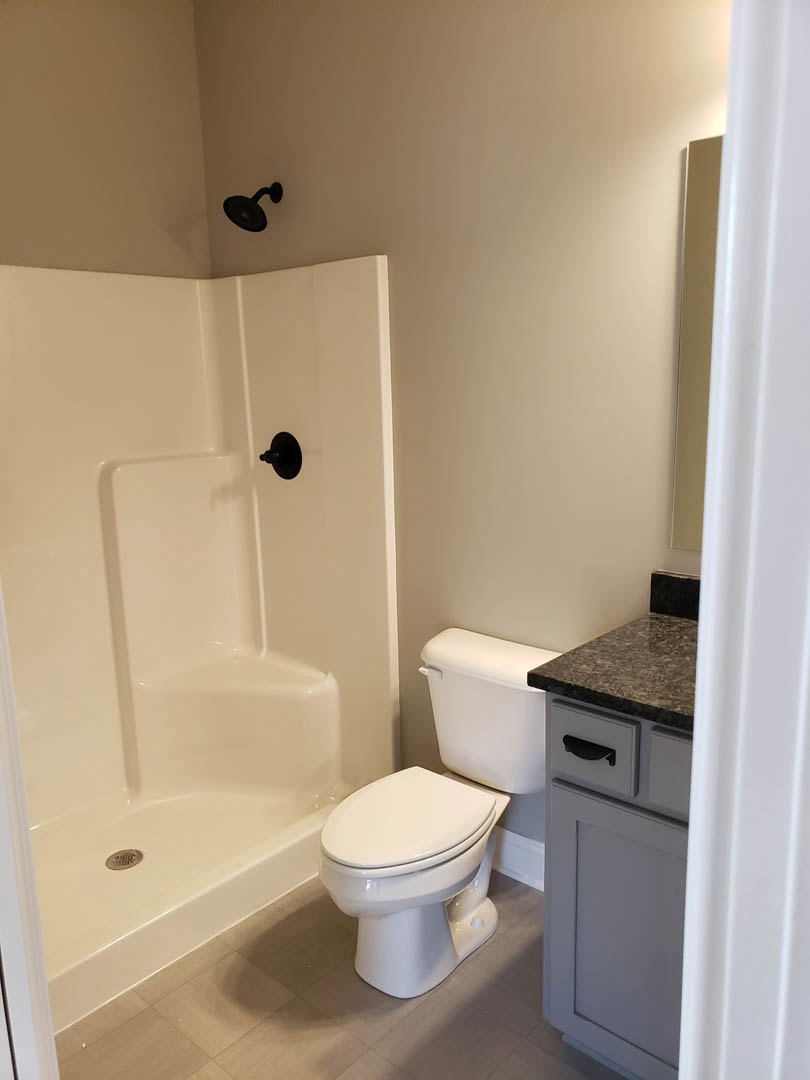 Modern bathroom with white toilet, black wall-mounted shower head, light tile walls, and white door partially visible