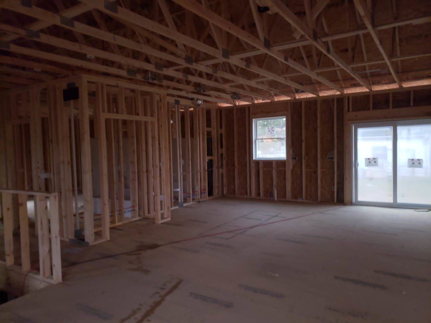 Living room with exposed wood ceiling beams, large window, glass door, light-colored flooring, and white sign on window.