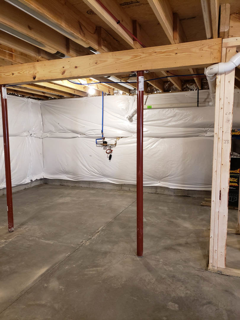 White-painted wall with exposed wood ceiling beam, light-colored floor, and visible building insulation along the ceiling.
