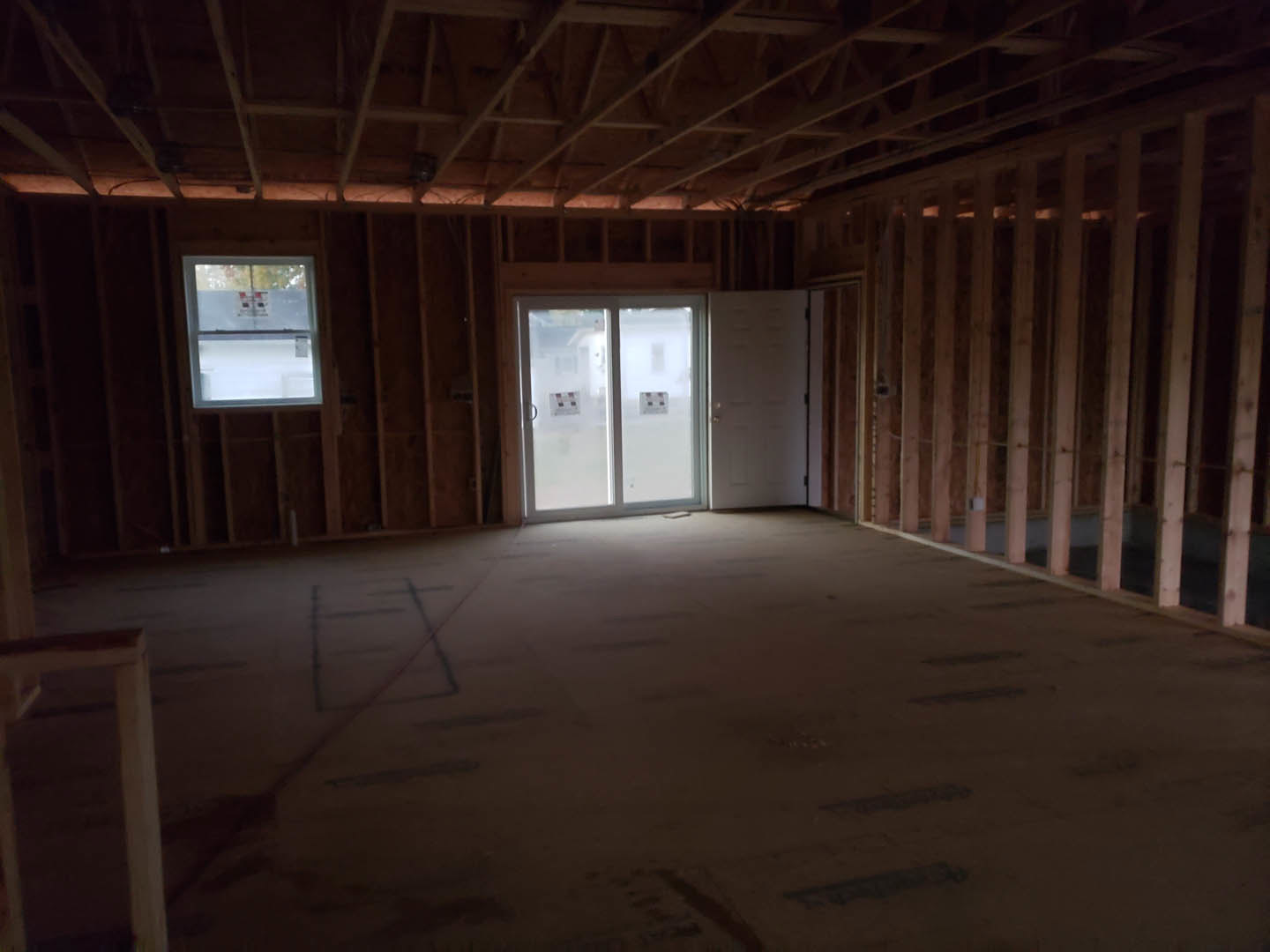 Spacious room with light wood flooring, exposed wooden ceiling beams, large glass door, and windows featuring stickers and signs