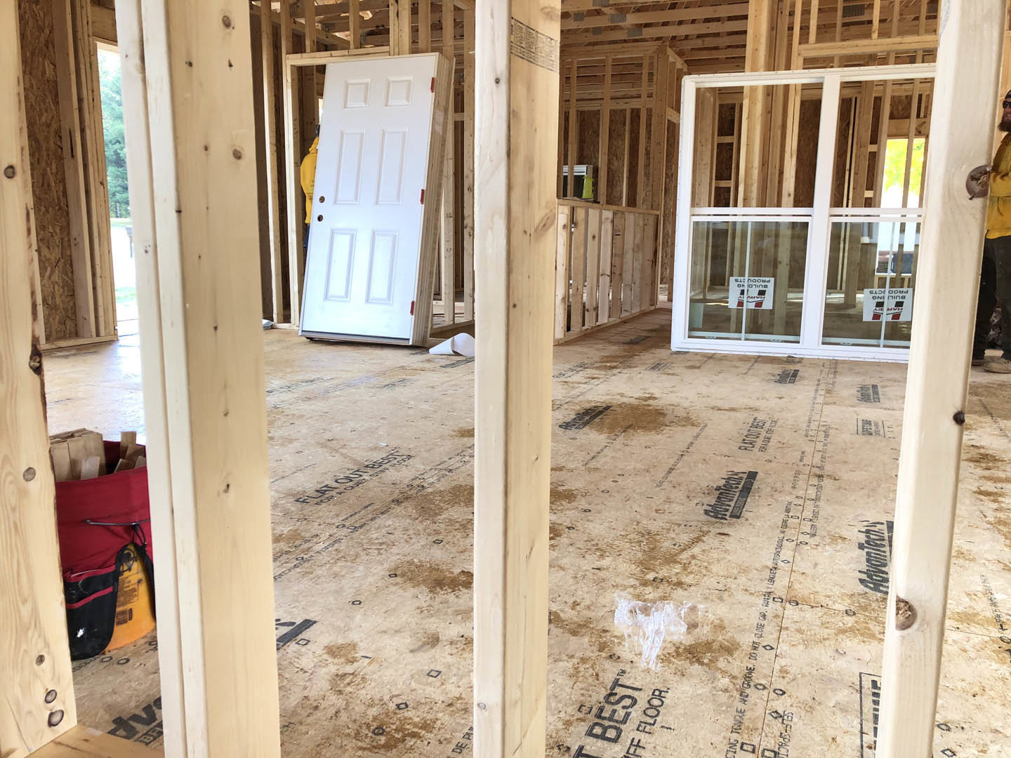 White paneled door in a wood frame next to a glass door, light-colored walls, visible construction materials and ladder in unfinished interior space