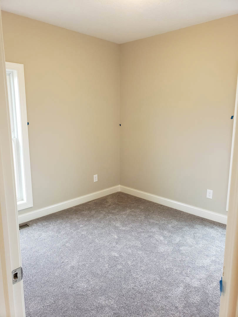 Carpeted room with white walls, open white door featuring a window, white ceiling, blue paint rollers resting against the wall