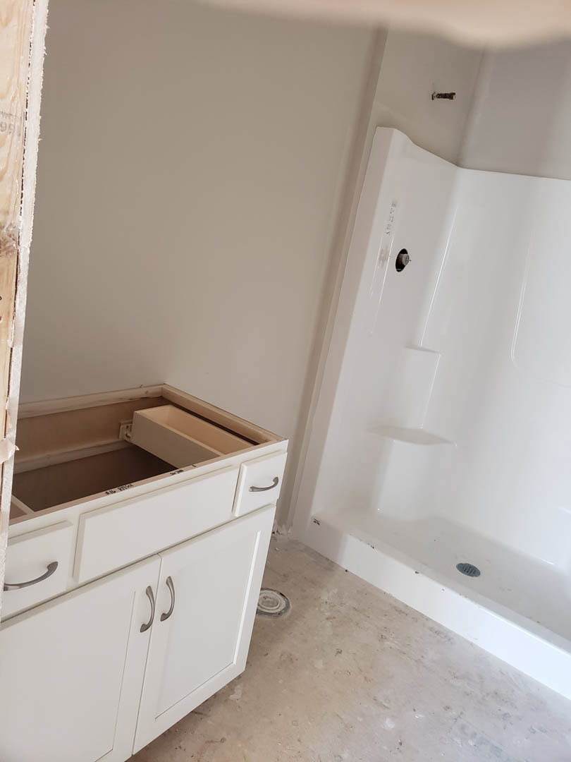 Bathroom with white tile shower, white sink set in a white vanity cabinet, chrome faucet, and light-colored walls.