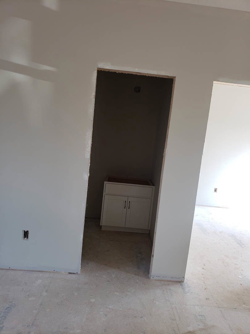 White bathroom with plaster walls, light wood flooring, white cabinet with drawer, and a closed door.