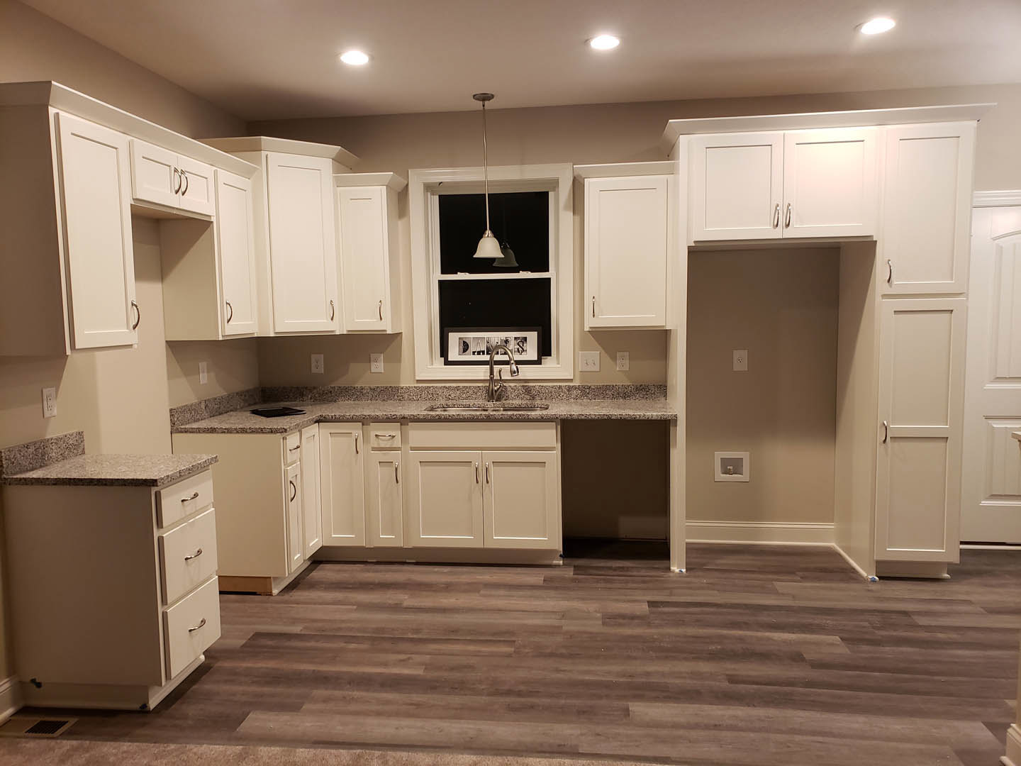 White kitchen with shaker cabinets, granite countertops, stainless steel appliances, wood flooring, recessed ceiling lights, and a central island with drawers.