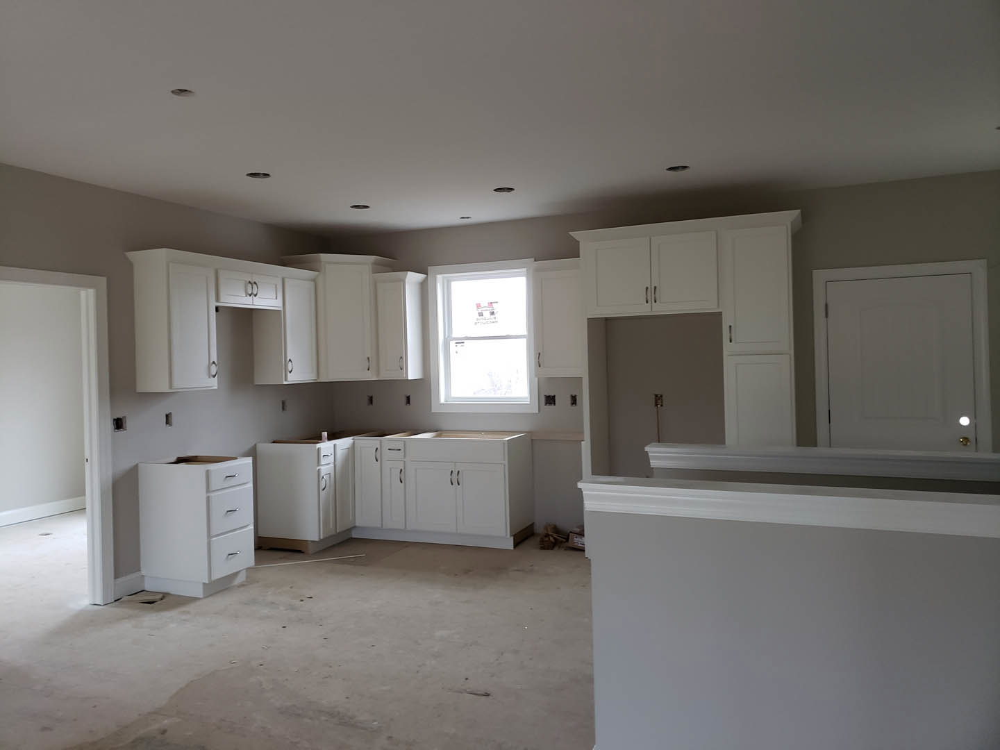 White kitchen with shaker cabinets, stainless steel sink under a window, light stone countertops, and hardwood flooring.