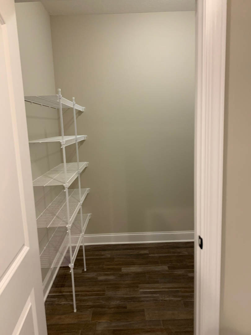 Closet with white shelving units, wood flooring, white door with black frame, metal shelf with white bars